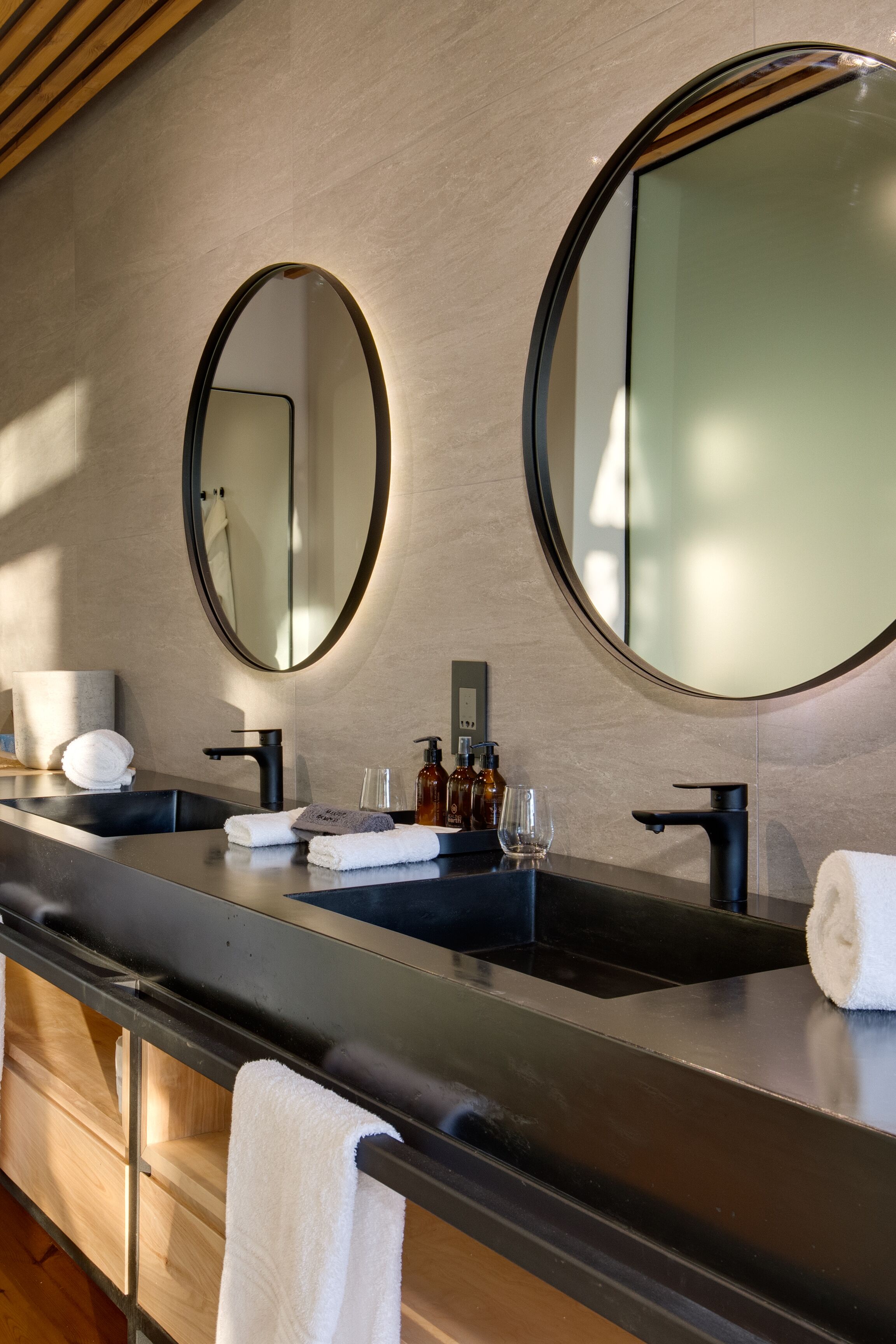 A modern bathroom with two sinks, large mirrors, and a wooden vanity.