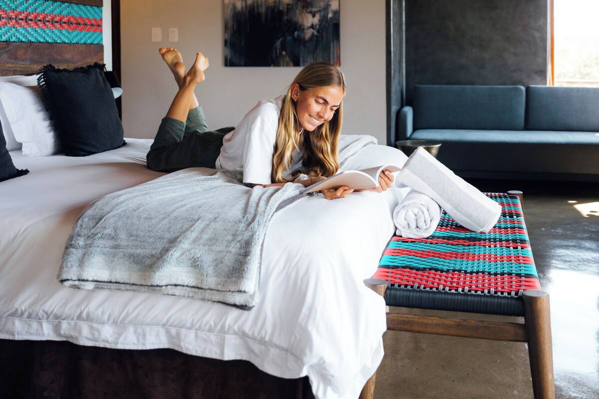 Une chambre à coucher avec un lit, un banc et une personne qui lit un livre.