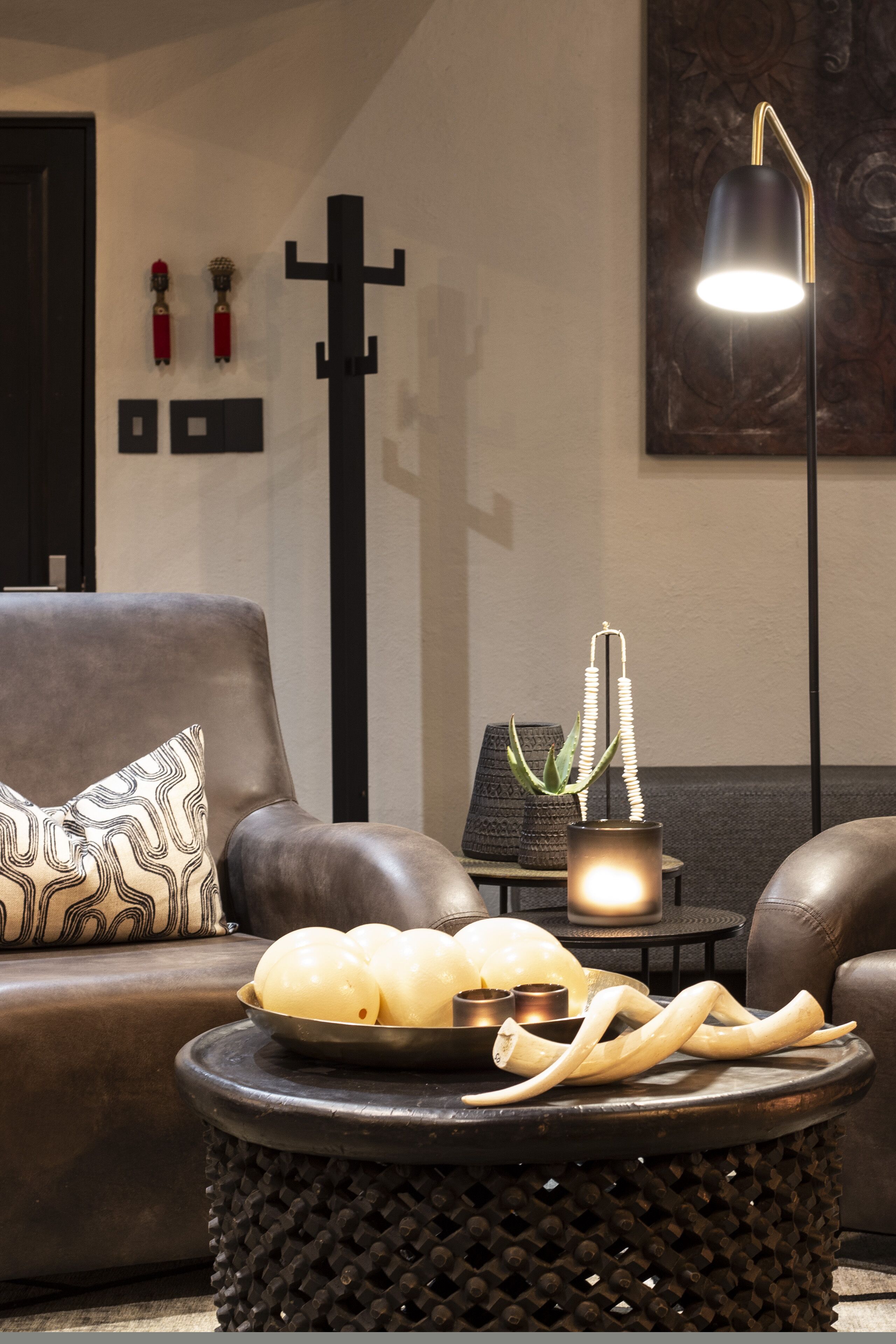 A modern living room with a leather sofa, a round black side table with decorative items, and a floor lamp.