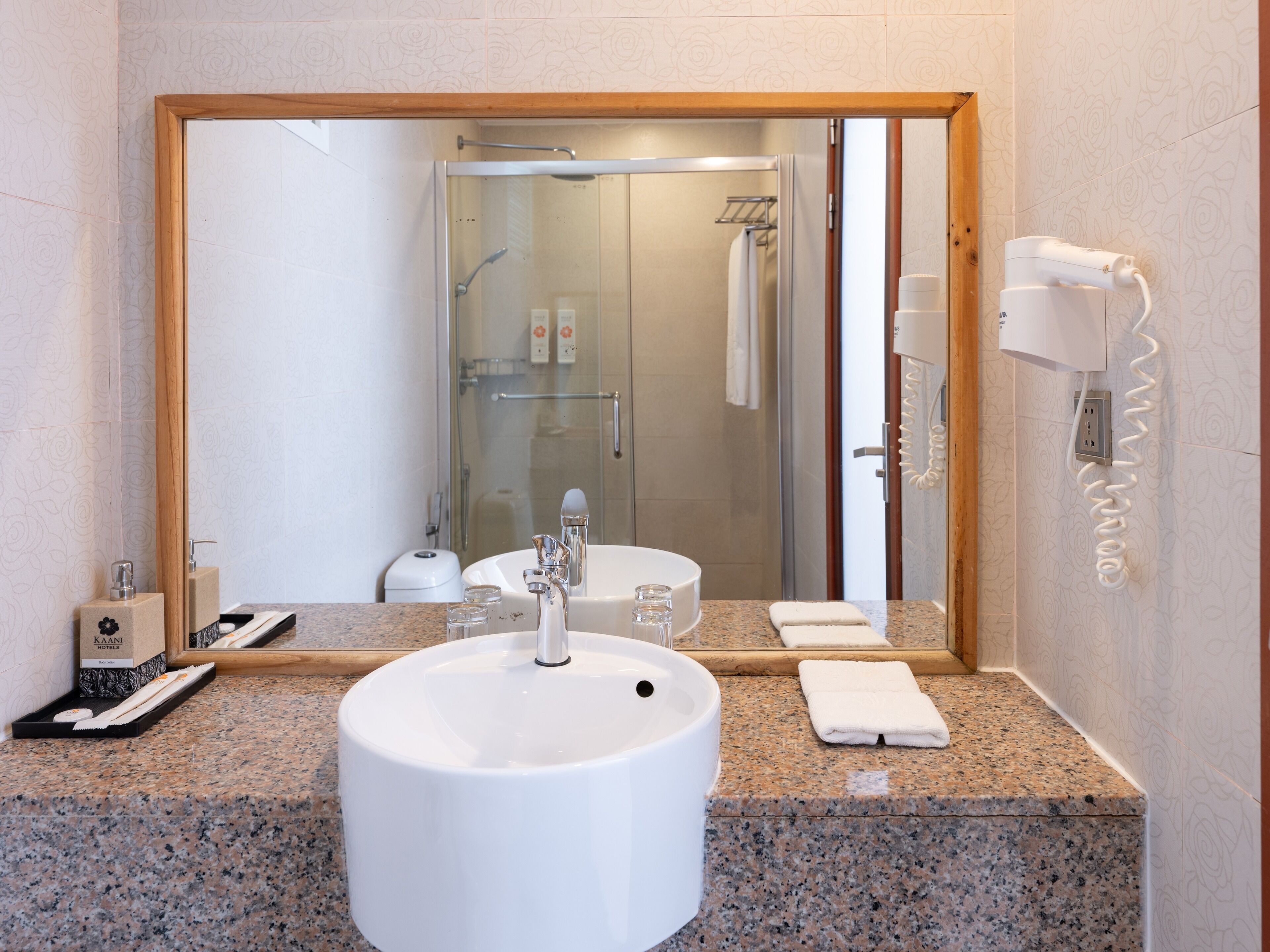 A bathroom with a sink, mirror, shower, and hairdryer.