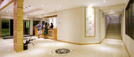 A spacious lobby with a reception desk, a staircase, and a decorative wall panel.