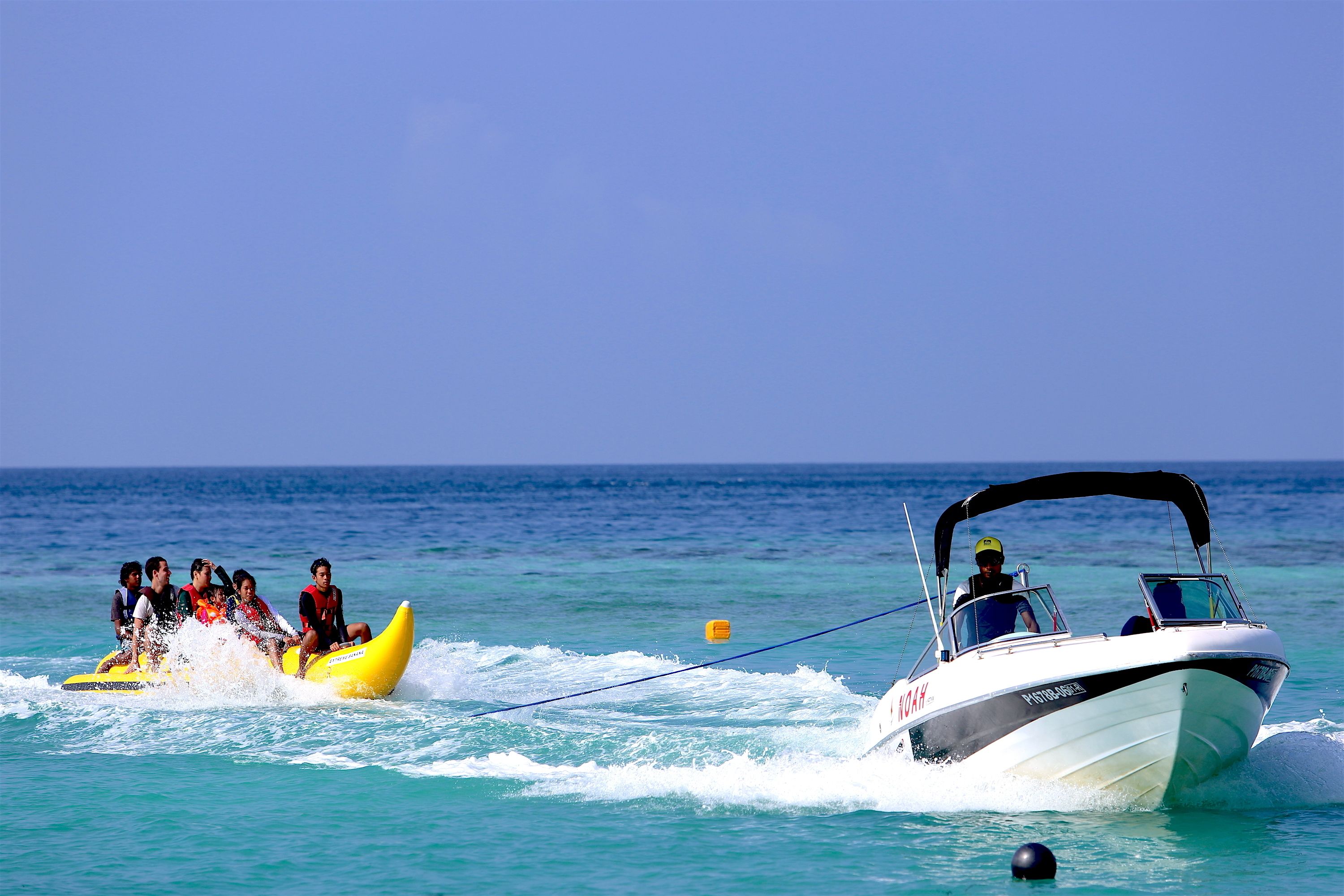 A boat towing a yellow raft with passengers, and a white boat with "NOAH" written on it.