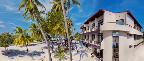 A beachfront hotel with a white facade, balconies, and palm trees.