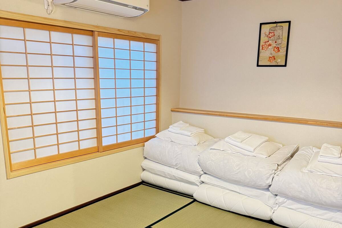 A traditional Japanese-style room with tatami flooring, a futon bed, a shoji screen window, and a ceiling fan.