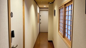 Un couloir doté d’un plancher en bois, une porte avec une plaque numérotée et une fenêtre à motifs géométriques.