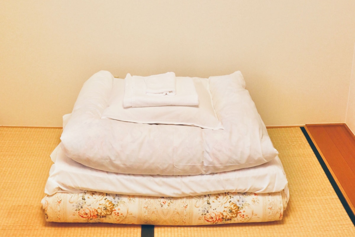 A neatly made bed with folded white linens and a floral-patterned mat.