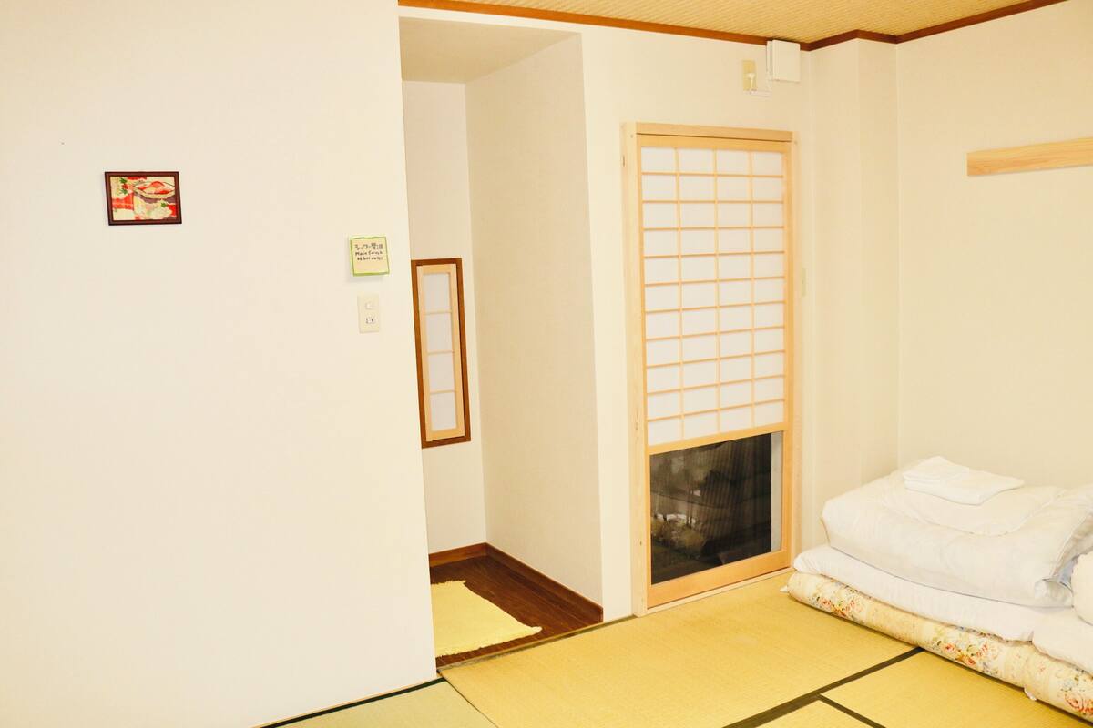 A traditional Japanese room with tatami flooring, a shoji screen door, and a futon bed.