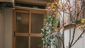 Une porte japonaise traditionnelle, un chemin de pierres et un petit jardin agrémenté d’un rocher et d’une statue.