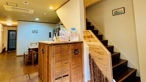 A wooden staircase leading to a second floor, a reception desk with informational signs, and a dining area with a wooden table and chairs. - Ikoi-no-ie (Kyoto)