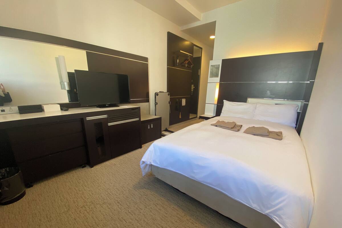 A hotel room with a bed, a desk with a television, a wardrobe, and a mirror.