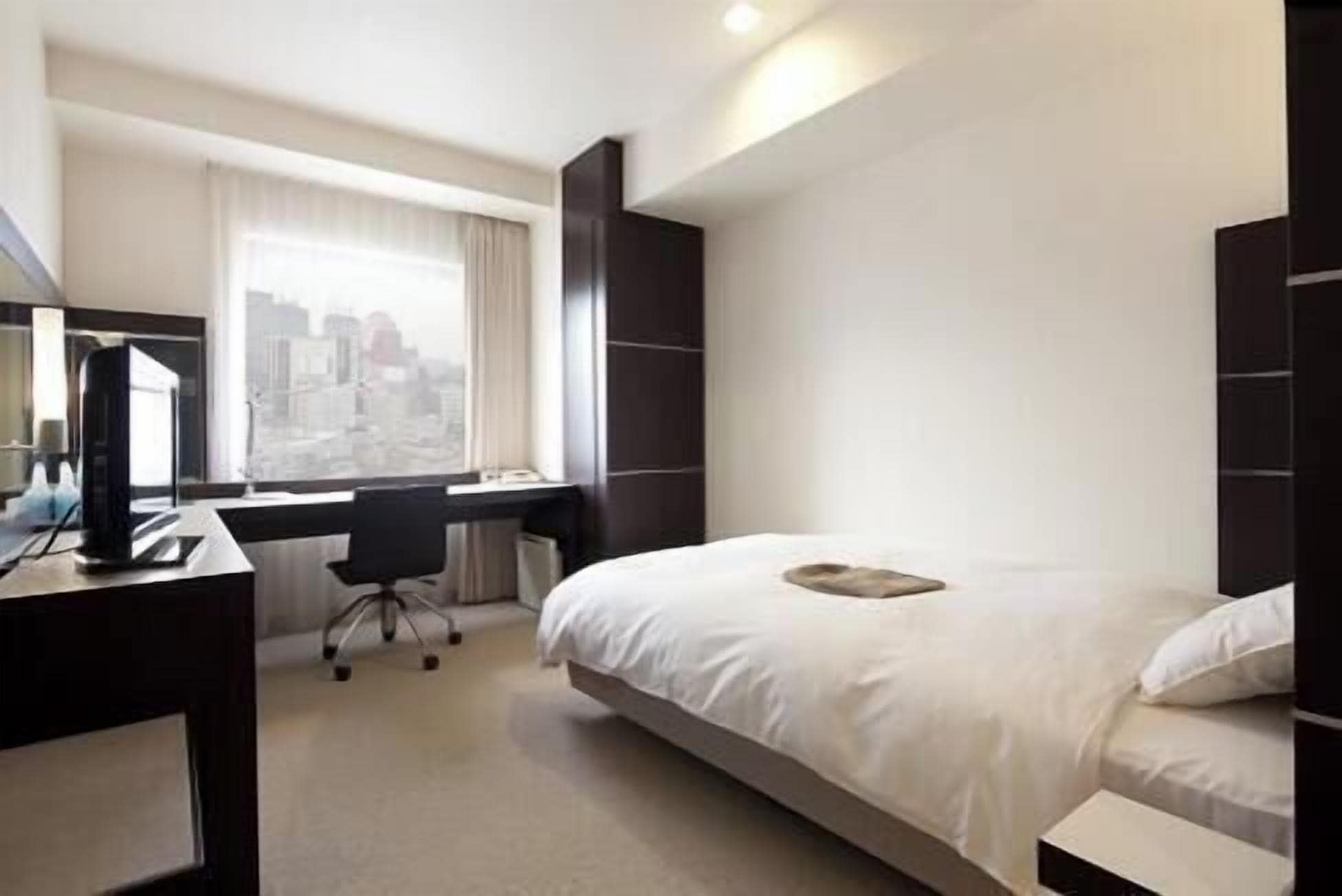 A hotel room with a bed, a desk, a chair, and a large window.