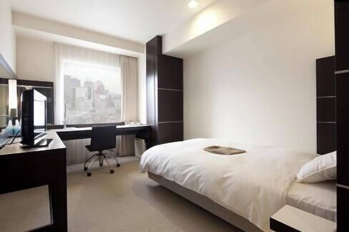 A hotel room with a bed, a desk, a chair, and a large window.
