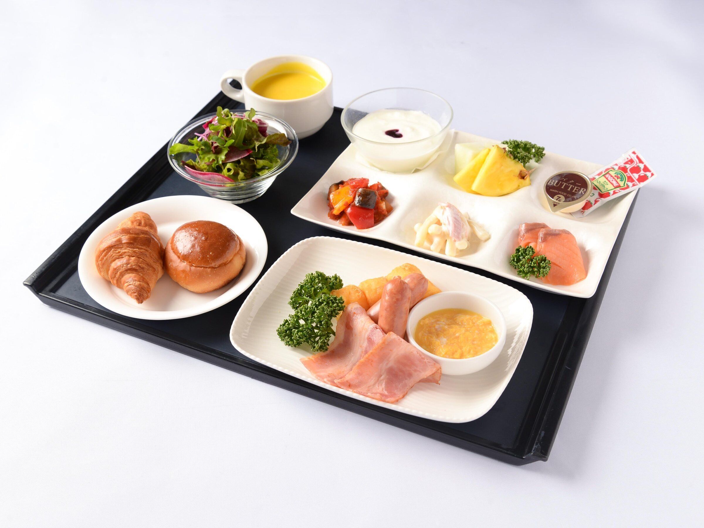 Una bandeja con croissants, ensalada, un tazón de sopa y varias carnes y salsas.