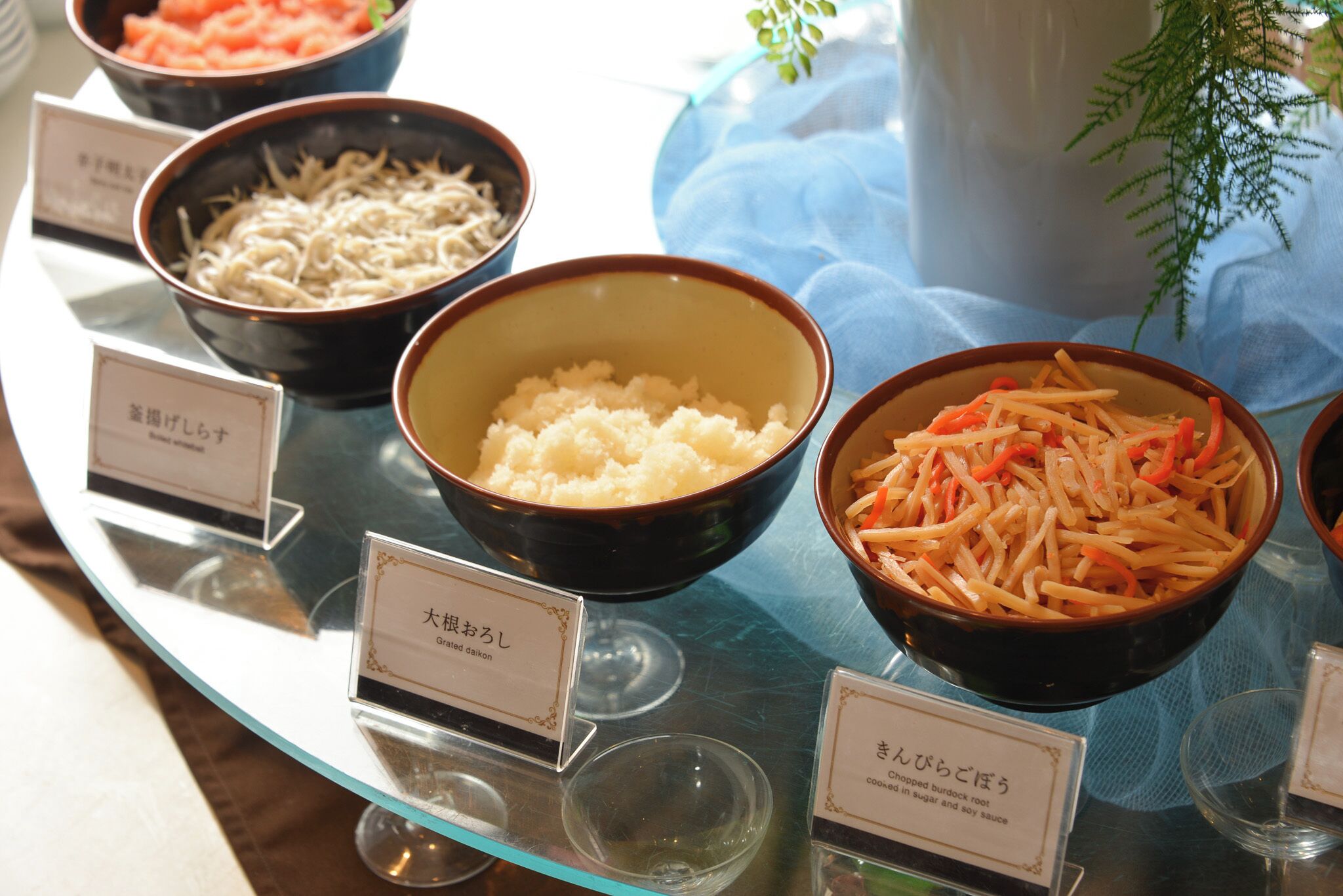 A buffet table with labeled bowls of food, including noodles, mashed potatoes, and a dish with carrots.