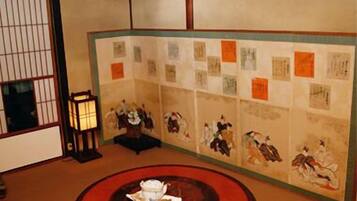 A traditional Japanese room with tatami flooring, a low table with a tea set, and a shoji screen with artwork.