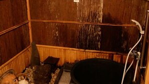 A rustic wooden room with a large black bathtub, wooden walls, and a small shelf with various items. - Kaikoan (Kyoto)
