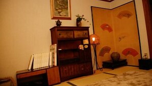 A traditional Japanese room with tatami flooring, a low wooden cabinet, a lamp, and a sliding door with decorative panels. - Kaikoan (Kyoto)