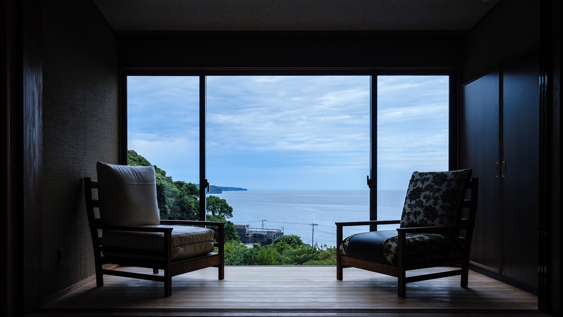 A room with two chairs facing a large window overlooking a body of water and greenery.