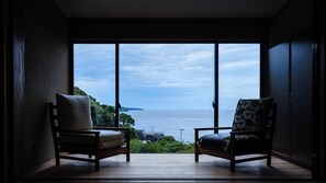A room with two chairs facing a large window overlooking a body of water and greenery.