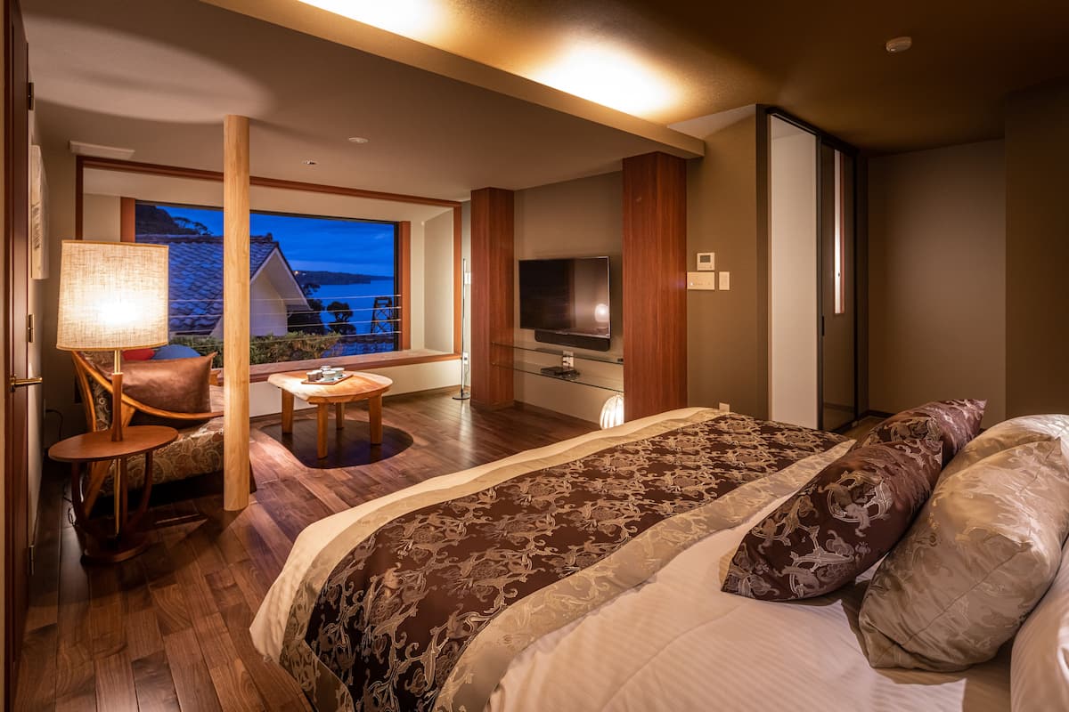 A modern hotel room with a large bed, a TV, a small table, and a view of the outside.