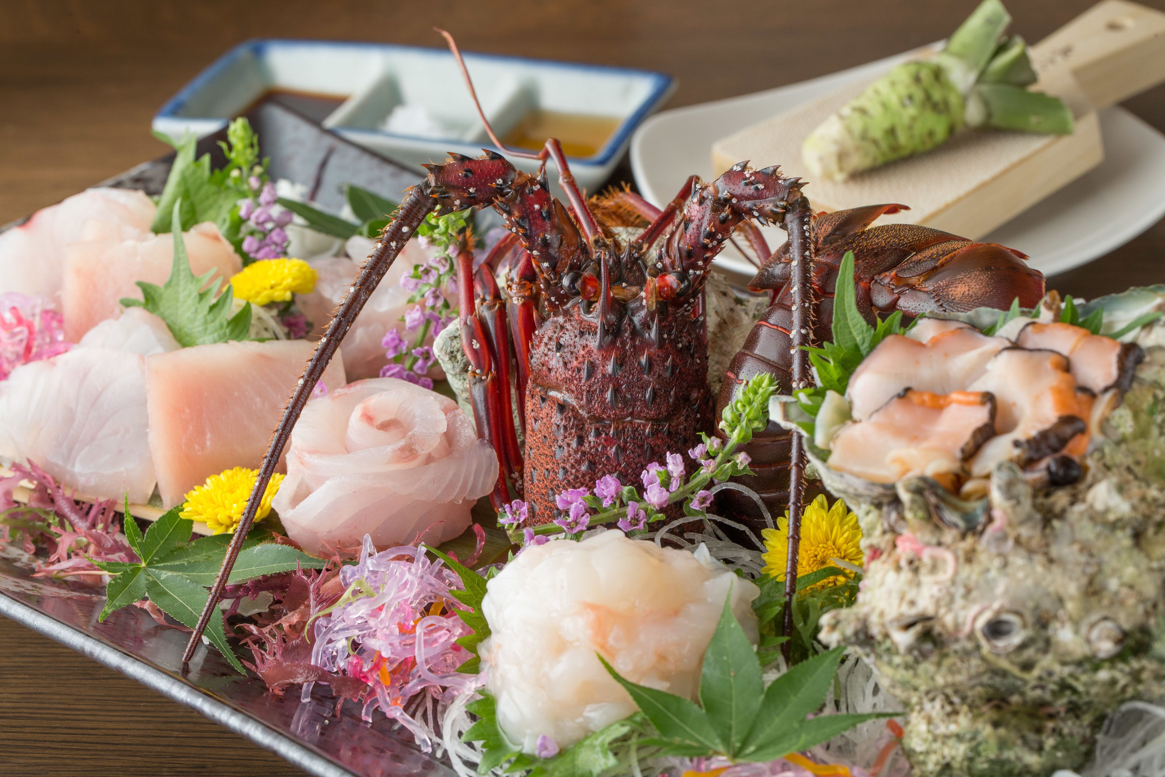 A seafood platter with various types of fish and a crab, garnished with flowers and seaweed.