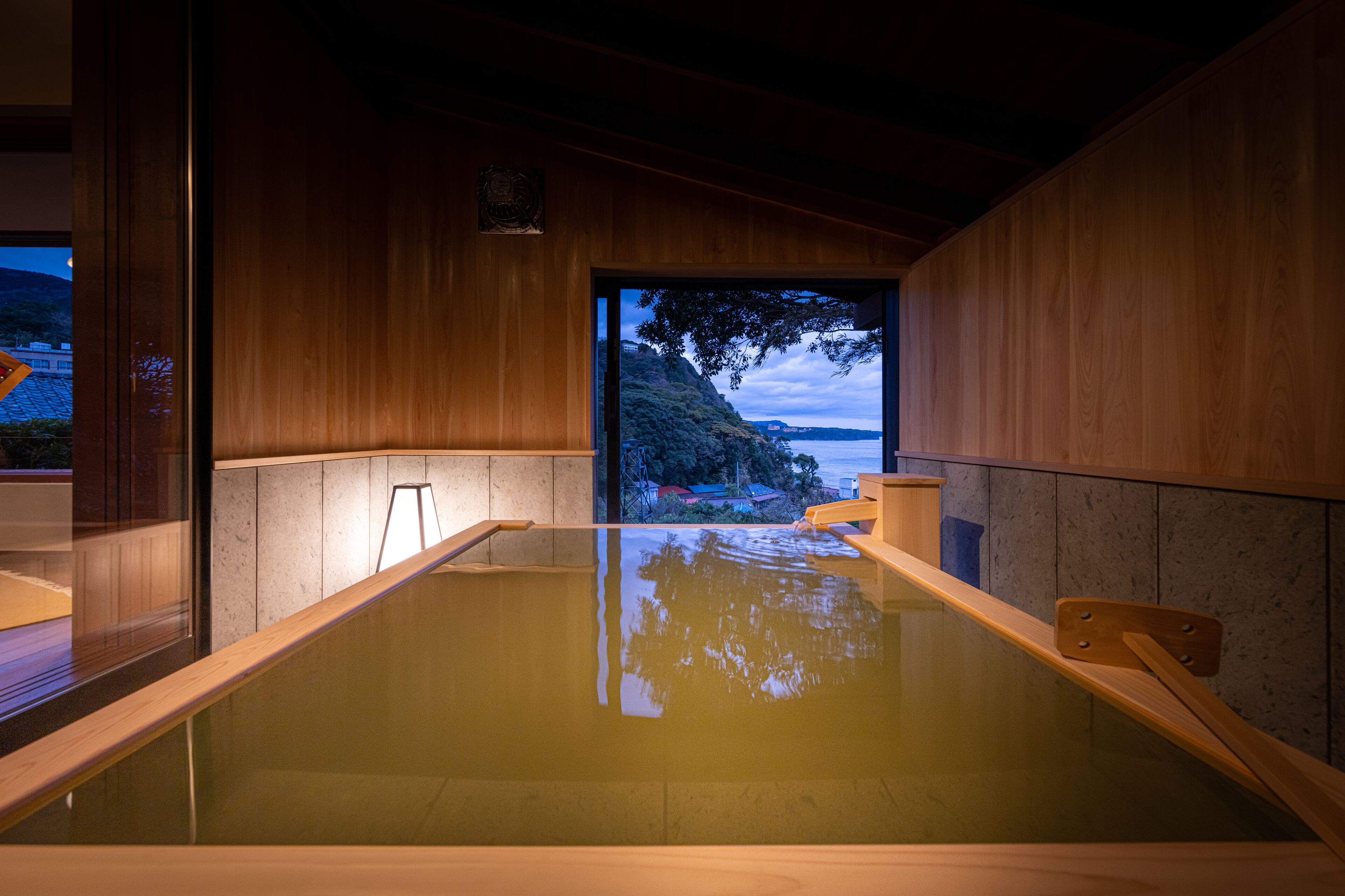 Een traditioneel Japans onsen met houten details, een omheinde hottub en uitzicht op een bergachtig landschap.
