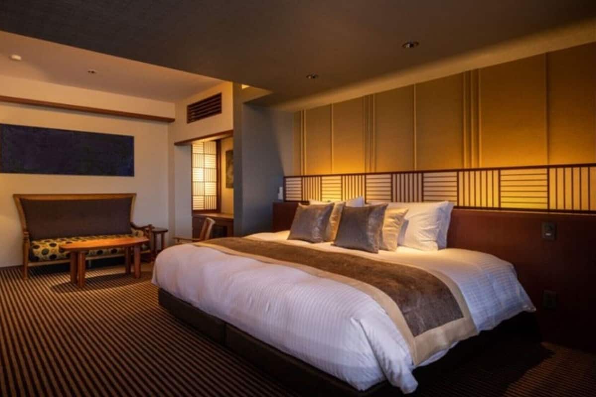 A hotel room with a large bed, a sofa, a desk, and a lamp.
