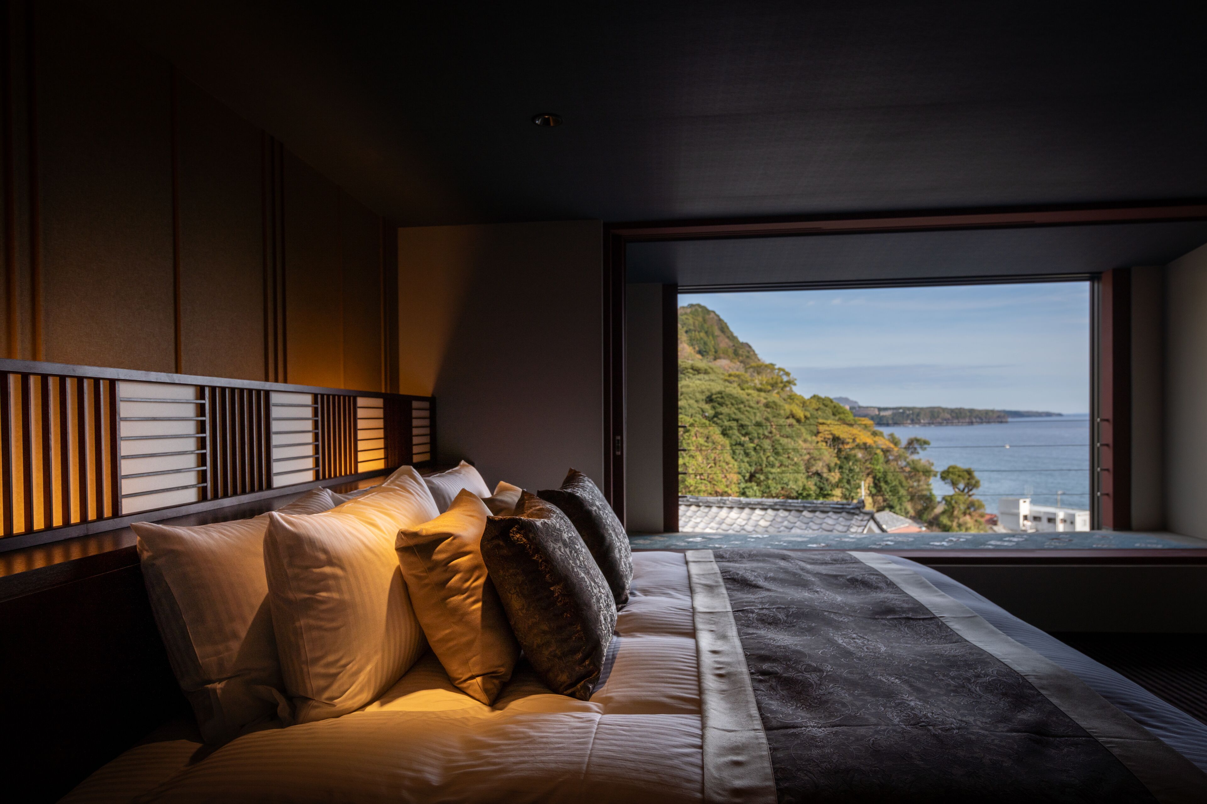 A bedroom with a large window offering a view of a coastal landscape.