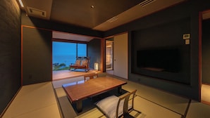 A traditional Japanese-style room with tatami flooring, a low table, a rocking chair, and a television. - Isaribi (Higashiizu)