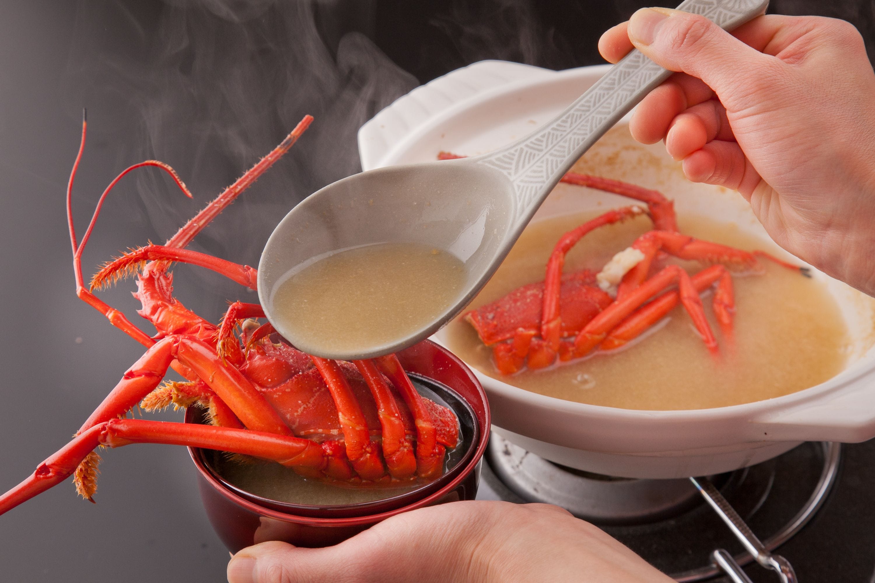 A person holding a bowl of soup with a red crab leg.