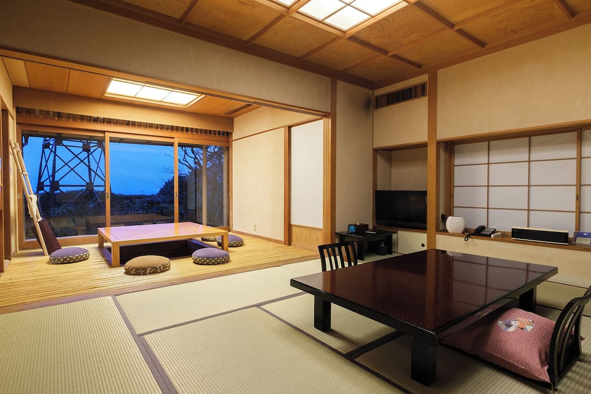A traditional Japanese-style room with tatami flooring, a low table, cushions, and a television.
