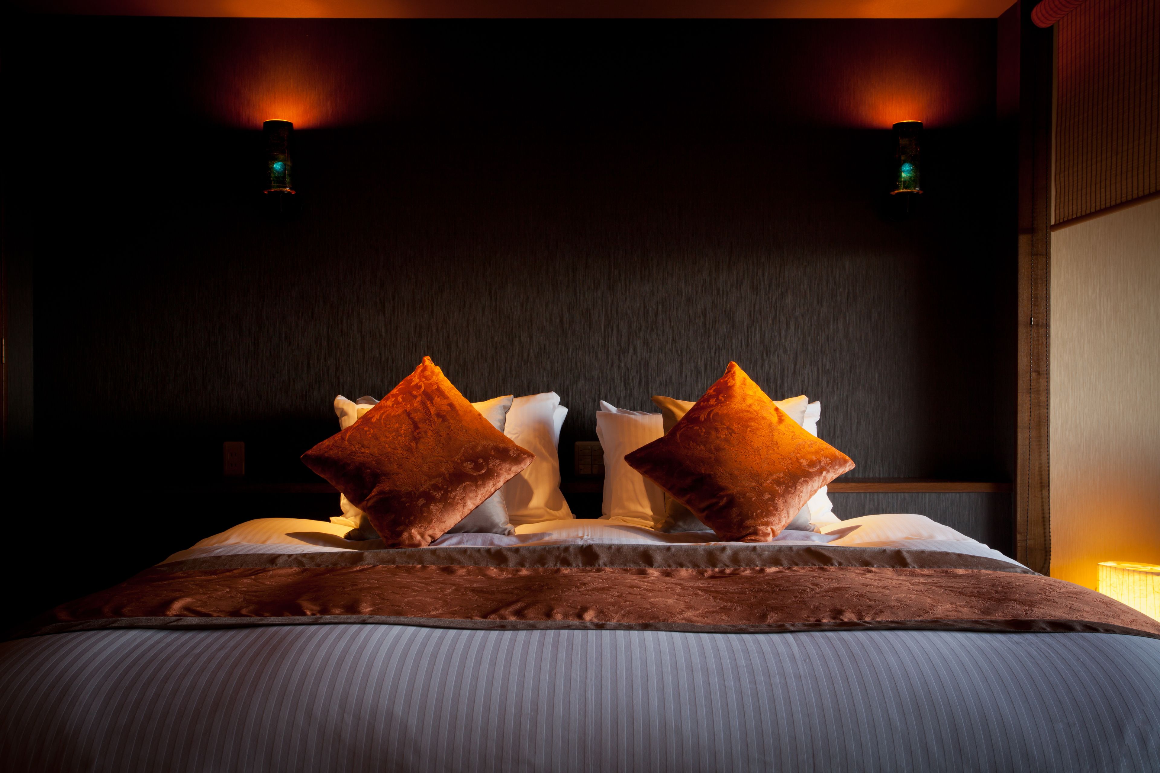 Una cama con dos almohadas grandes, un edredón a rayas y dos luces fijadas a la pared.