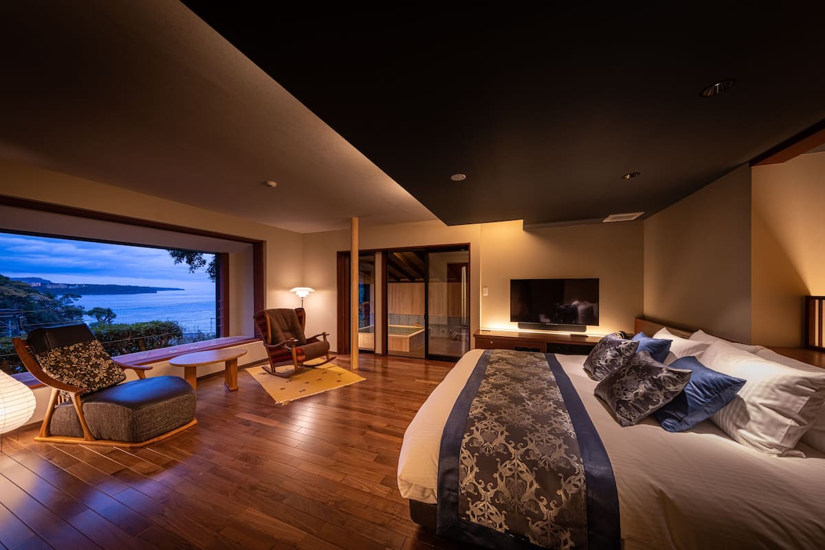 A modern bedroom with a large bed, a TV, and a view of the sea.