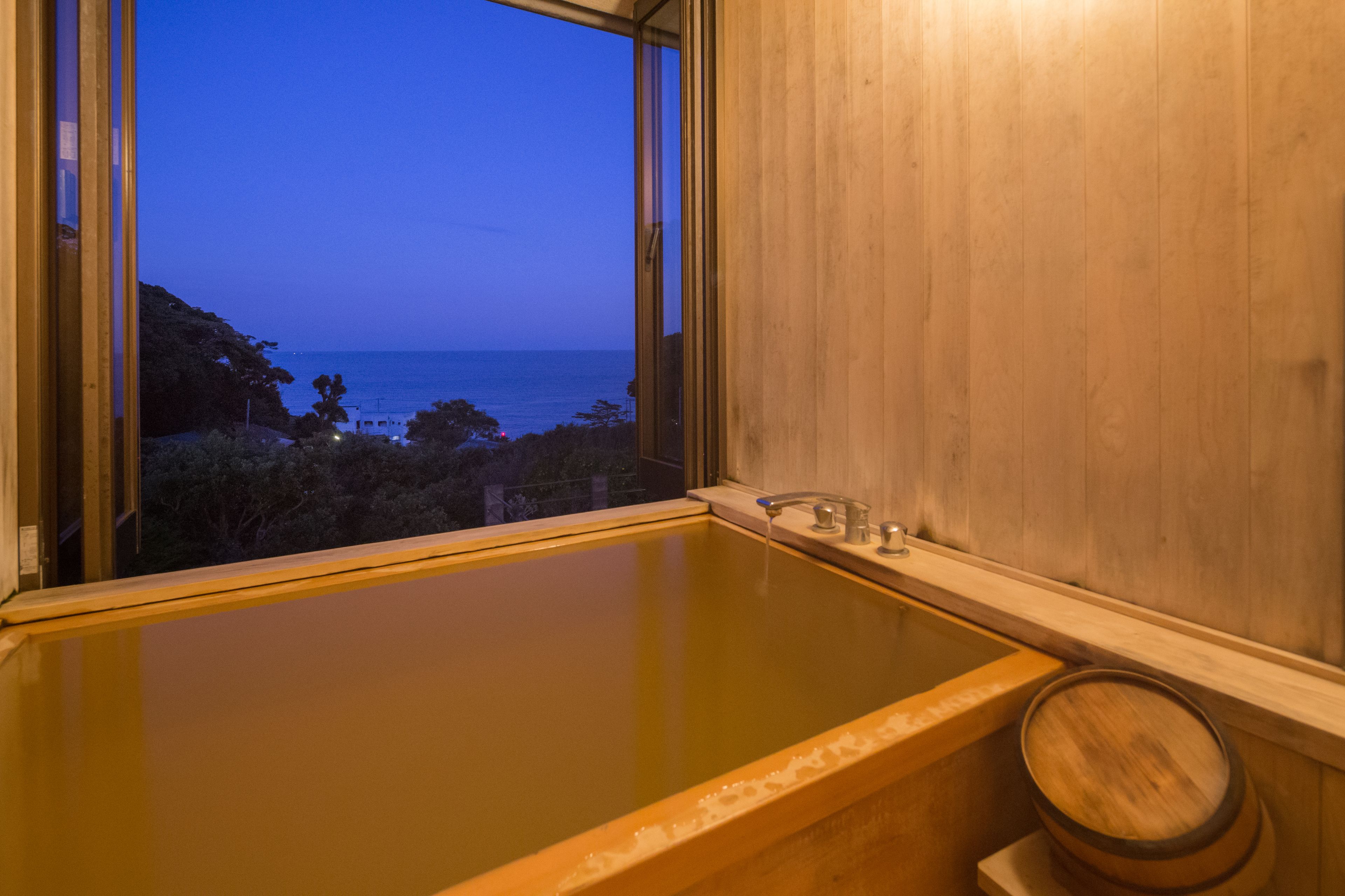 A wooden bathtub with a view of the sea through a window.