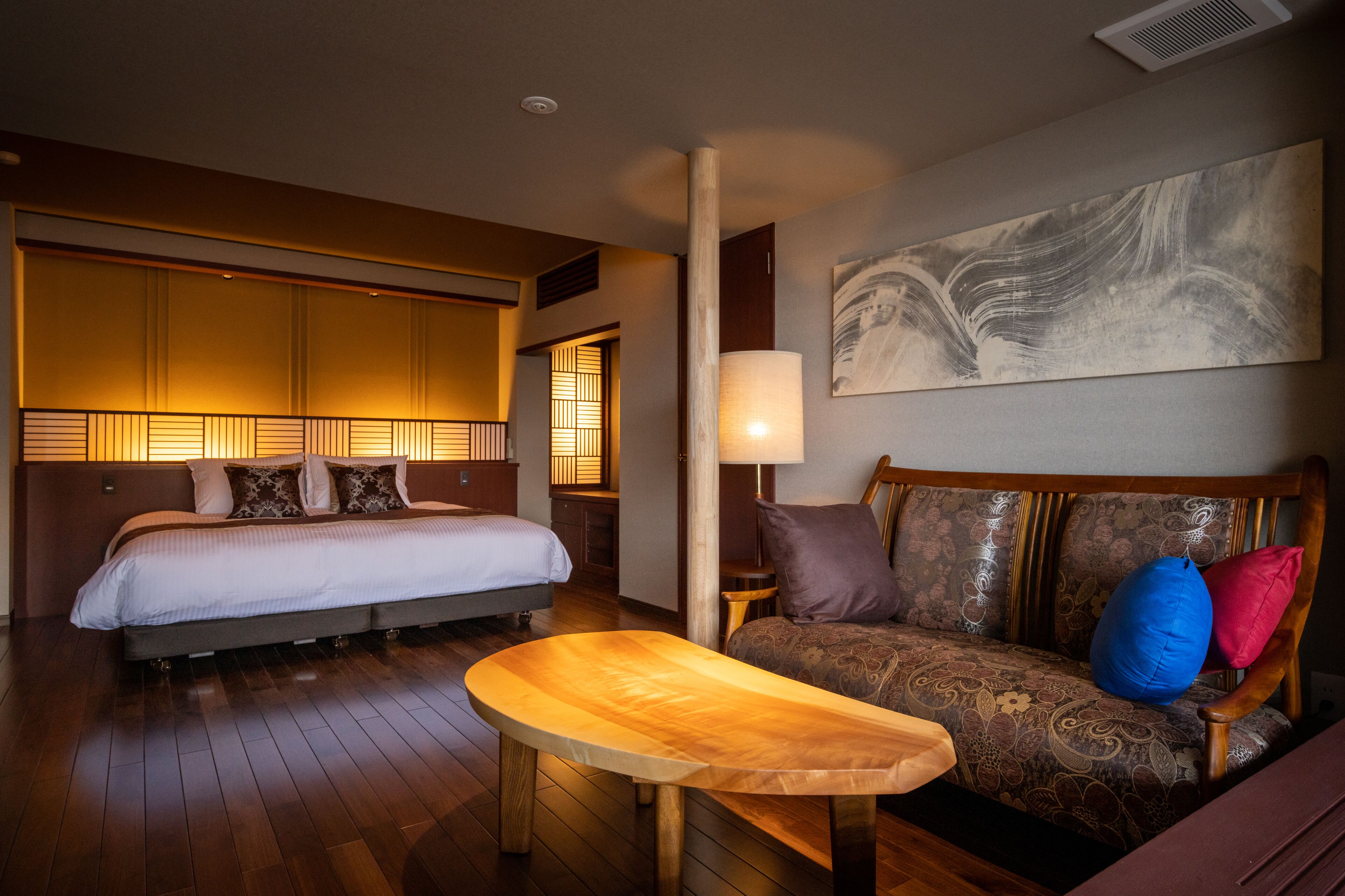 Een hotelkamer met een bed, een slaapbank, een houten bijzettafeltje en een schilderij aan de muur.