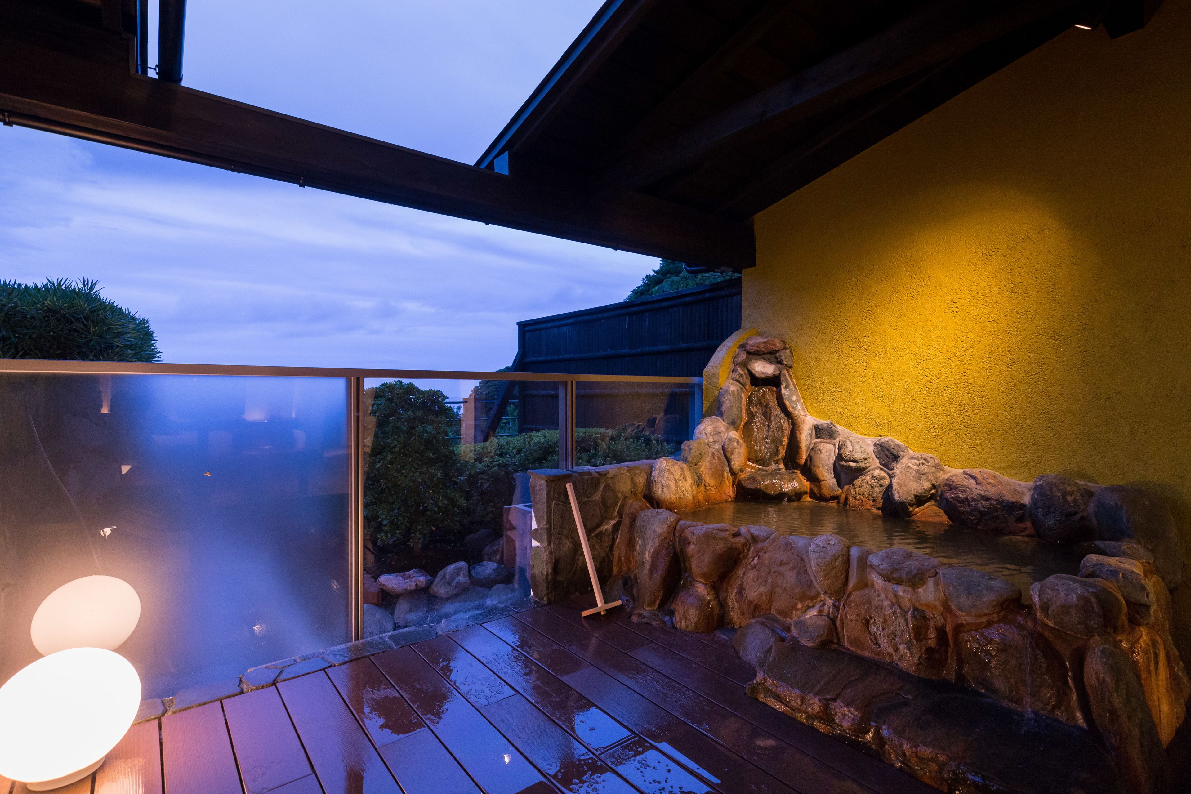 Une terrasse en bois agrémentée d’un élément décoratif aquatique en pierre et d’une structure en verre.