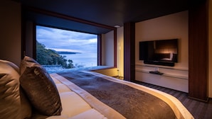 A modern bedroom with a large window, a flat-screen TV mounted on the wall, and a bed with a headboard. - Isaribi (Higashiizu)