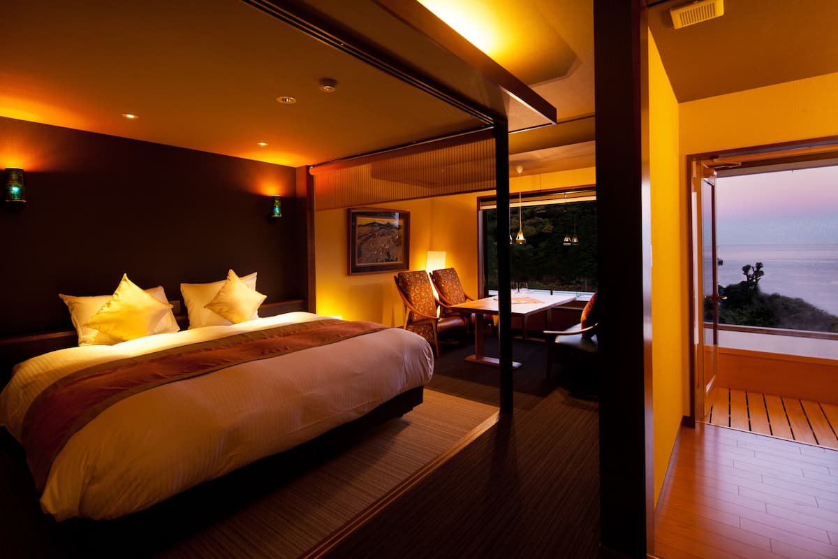 A modern hotel room with a large bed, a dining area, and a balcony with a view.