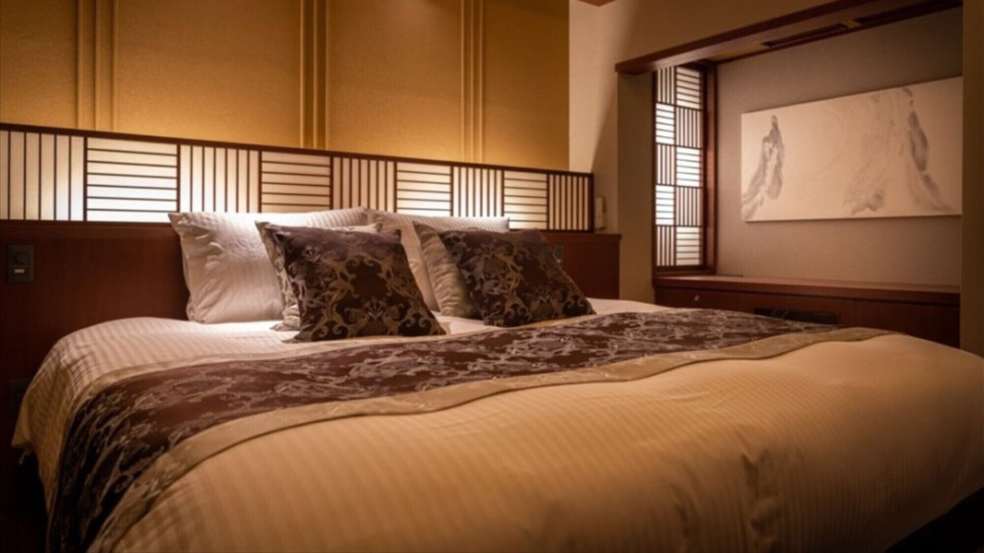 Una cama bien arreglada con almohadas estampadas, un cabecero de madera y una pared con una obra de arte enmarcada.