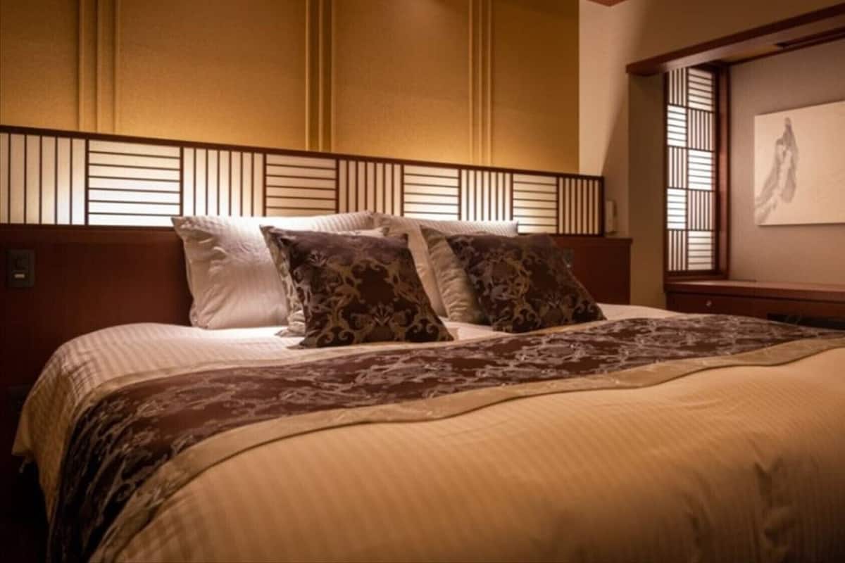 A neatly made bed with patterned pillows, a wooden headboard, and a wall with a framed artwork.