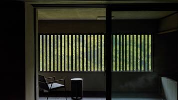 Una habitación con vista al exterior, visible a través de una ventana con persianas verticales, una silla y una pequeña mesa redonda.
