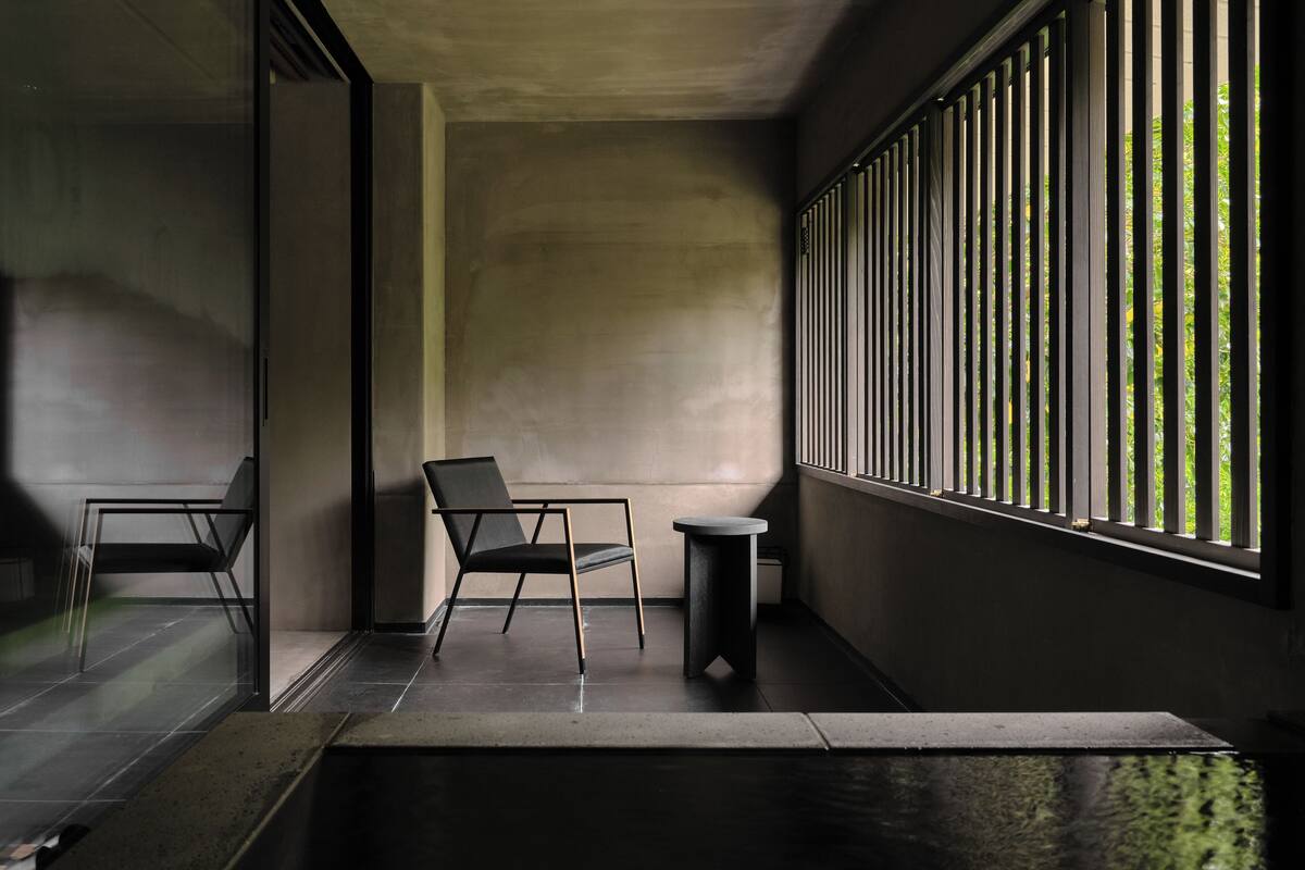 A modern interior with a minimalist design, featuring a single chair and a small table near a window with vertical blinds.
