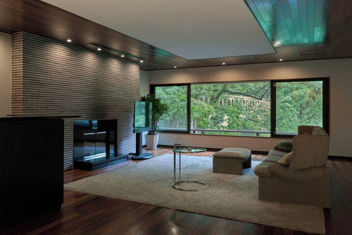 A modern living room with a fireplace, large windows, and a view of greenery.
