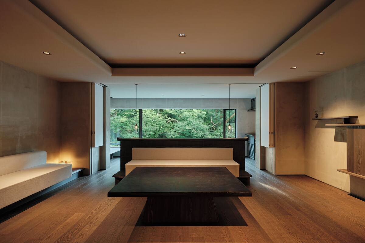 A modern interior with a central seating area, large windows offering a forest view, and a minimalist design.