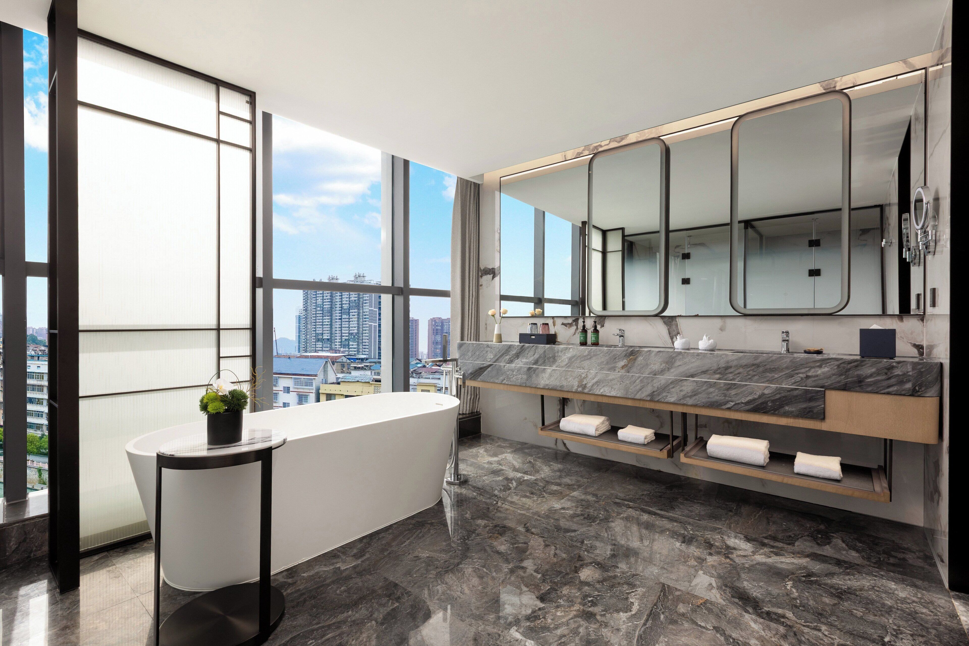 A modern bathroom with a large bathtub, a vanity with a marble countertop, and a large mirror.