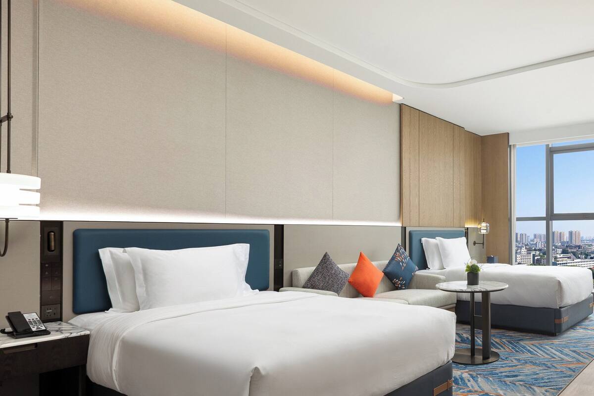 A hotel room with a large bed, a smaller sofa, a round table, and a city view through the window.