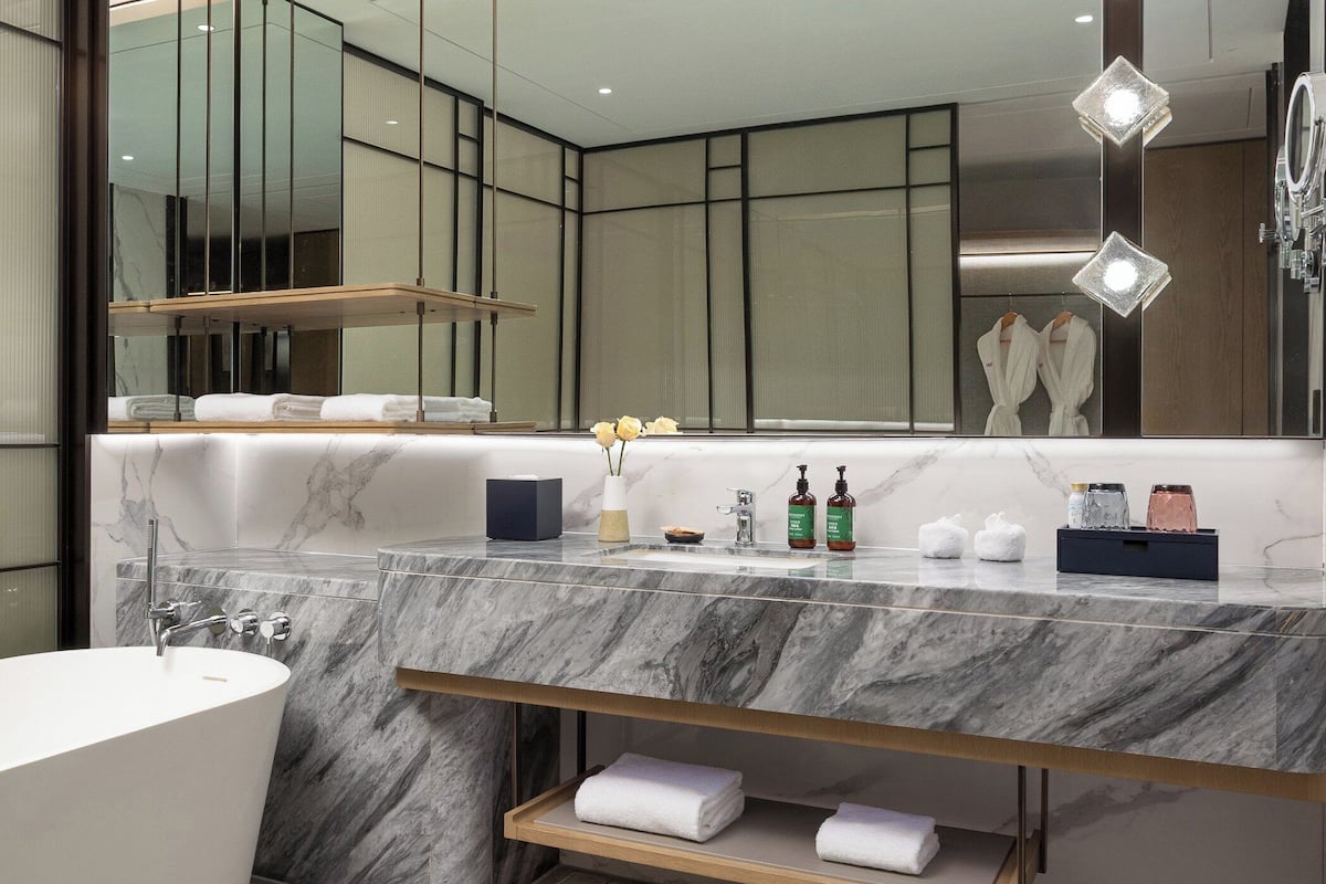 A modern bathroom with a marble vanity, a freestanding bathtub, and a large mirror with integrated lighting.