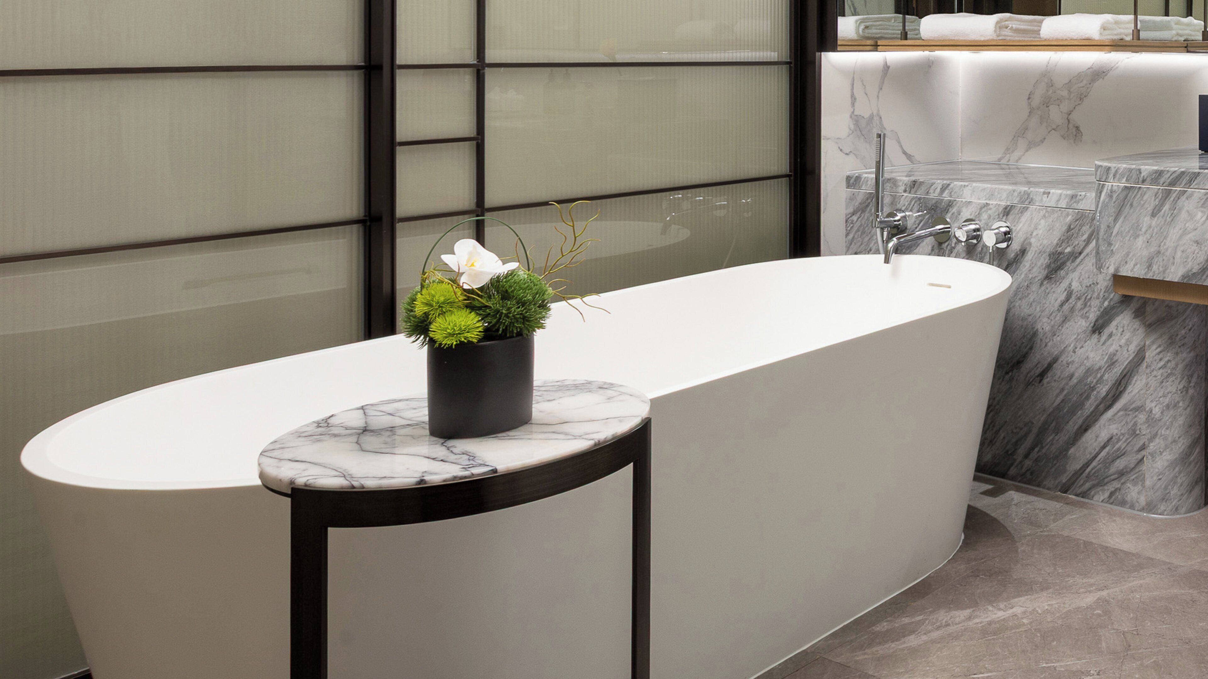 A modern bathroom with a freestanding bathtub, a marble countertop, and a potted plant.