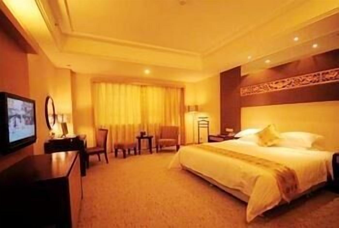 A hotel room with a large bed, a desk, a chair, a TV, and a window with curtains.