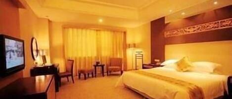A hotel room with a large bed, a desk, a chair, a TV, and a window with curtains.